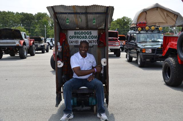 Man seated in a wooden booth labelled Bigdogs Offroad, with off-road vehicles behind him