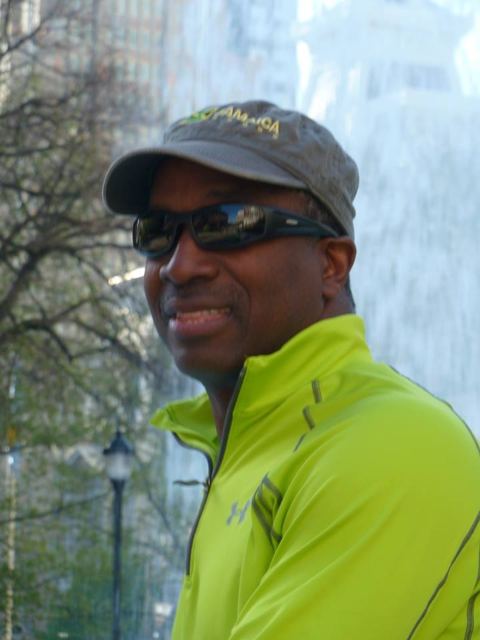 Man in a cap and sunglasses wearing a lime-green jacket outdoors