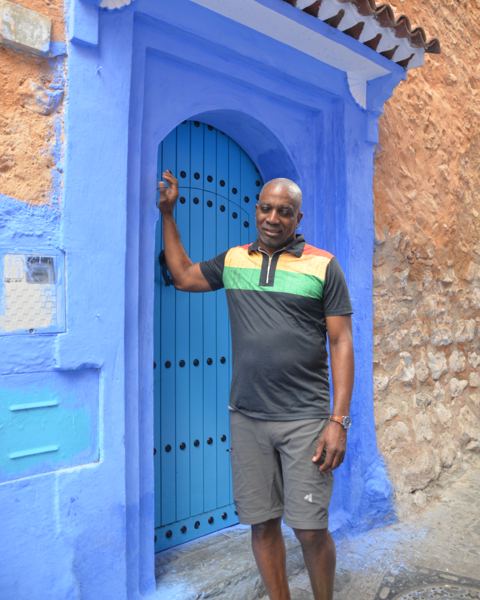 Man in a green, yellow and red striped shirt resting a hand on a blue door