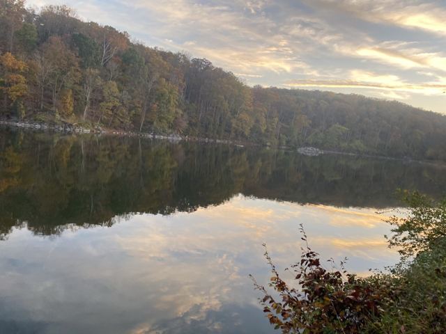 Still river with wooded hills and a stone wall along a towpath at dusk