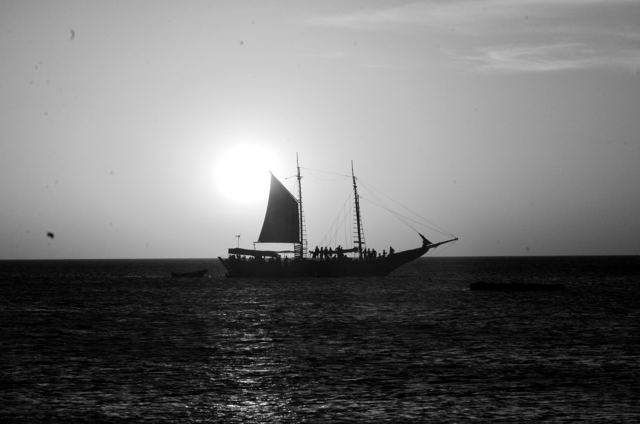 A sailing ship in silhouette against an orange sunset