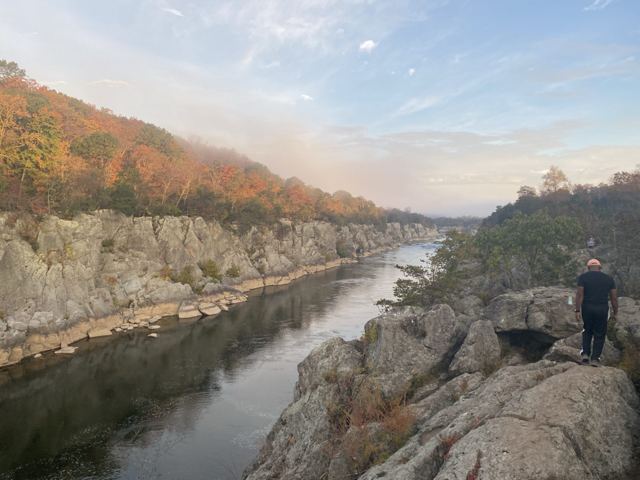 Man standing on rocks beside a calm river gorge in autumn