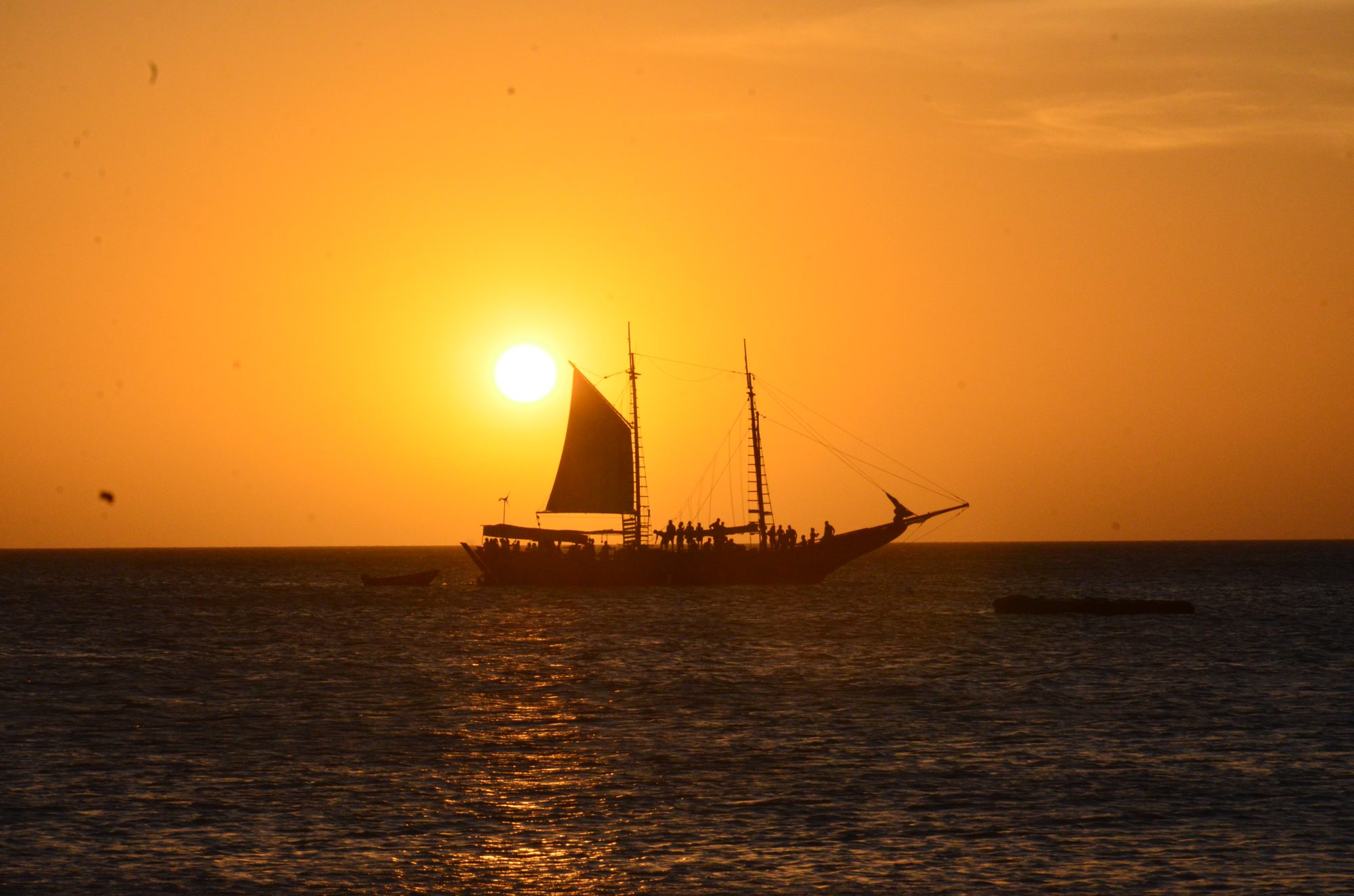 A sailing ship in silhouette against an orange sunset