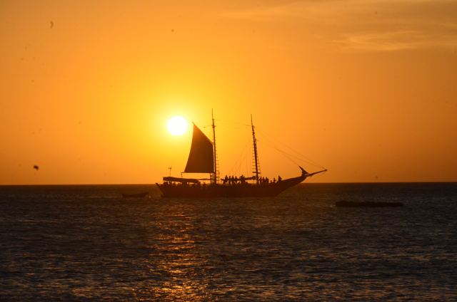 A sailing ship in silhouette against an orange sunset
