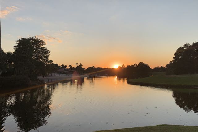 Sunset over a calm pond lined with trees on a golf course