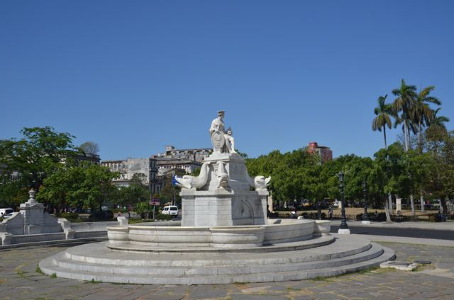 A white statue on a round fountain in a plaza