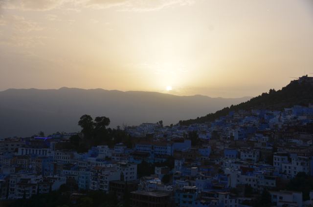 Sun setting behind hazy mountains above the blue town