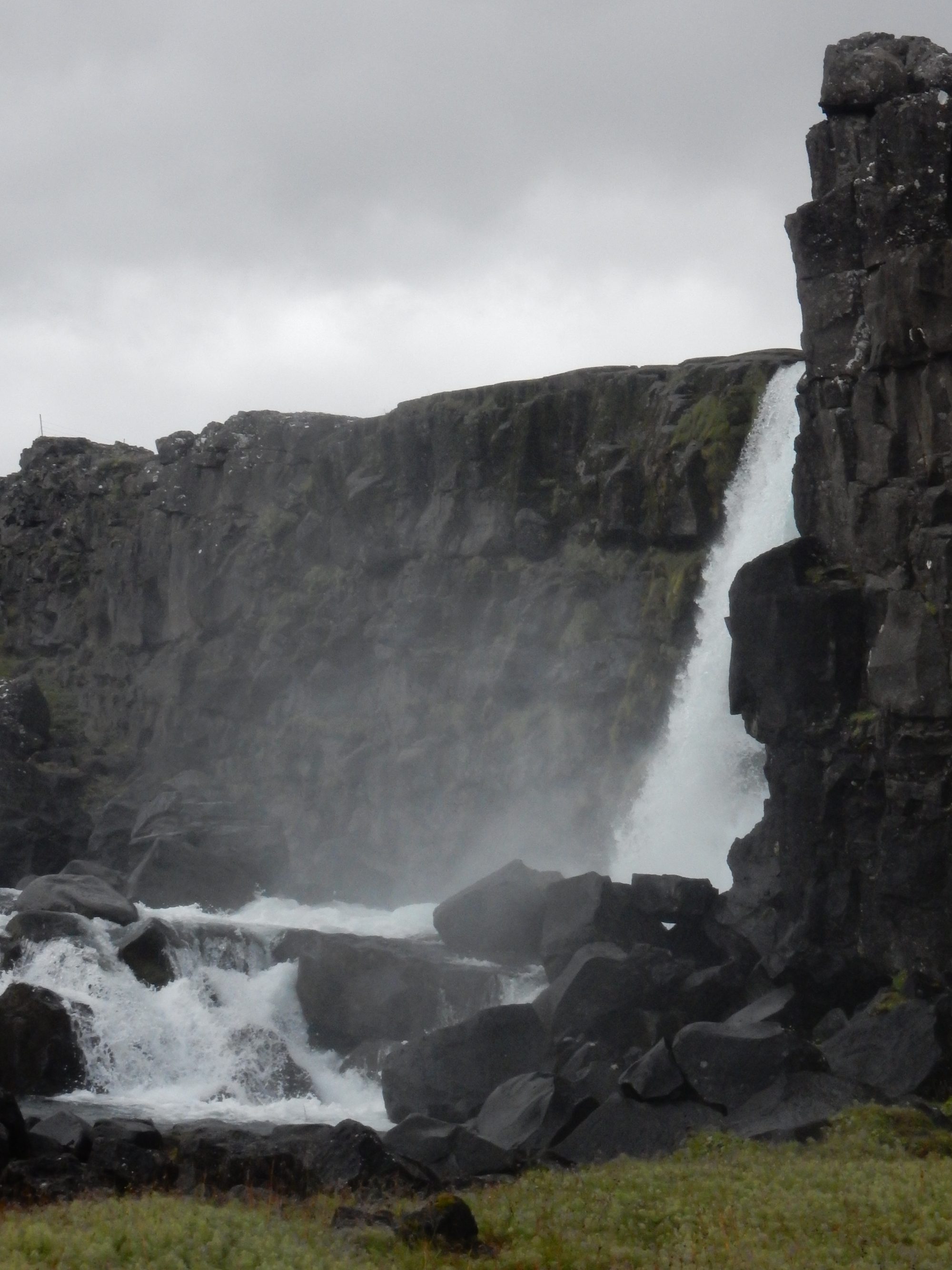A waterfall dropping beside a dark basalt cliff