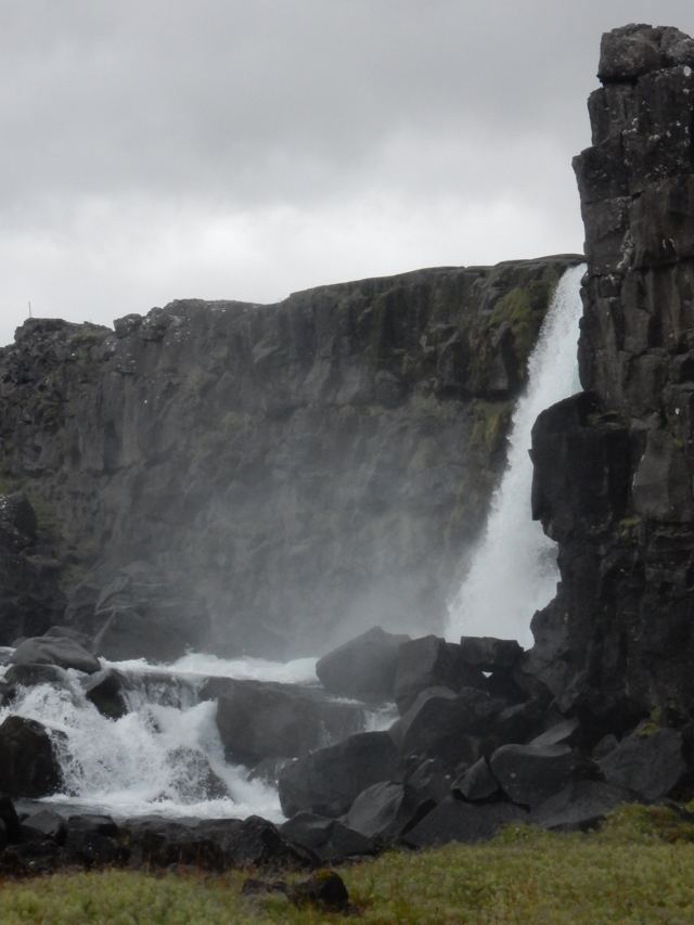 A waterfall dropping beside a dark basalt cliff