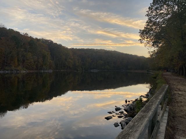 Still river with wooded hills and a stone wall along a towpath at dusk