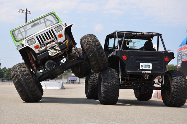Two modified off-road Jeeps with oversized tyres, one tilted up on a front wheel