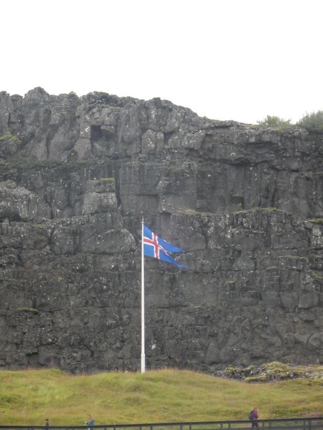 The Icelandic flag flying beside a rock wall
