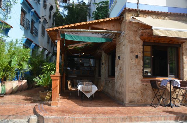 A stone cafe with an awning and tables